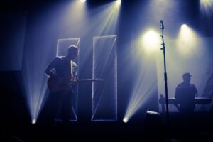 Live-Bühne mit Gitarrist, Keyboarder und synchron wirkenden Lichtstrahlen