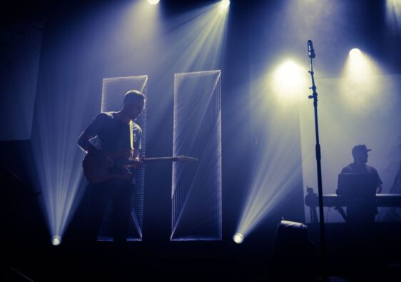 Live-Bühne mit Gitarrist, Keyboarder und synchron wirkenden Lichtstrahlen